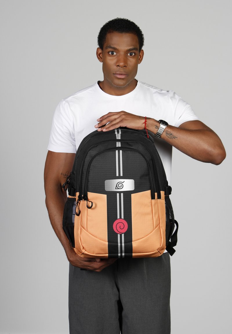 Mochila negra y naranja con un logo, que cuenta con dos franjas verticales y múltiples bolsillos. El material parece resistente con un acabado texturizado.