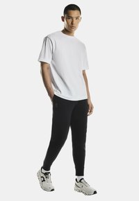Witte katoenen t-shirt, comfortabele pasvorm, gecombineerd met zwarte taps toelopende joggers. Schoeisel heeft een mix van witte en zwarte accenten, lichtgewicht ontwerp.