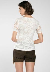 Weißes Spitzen-T-Shirt mit kurzen Ärmeln, Blumenmuster und rundem Ausschnitt, kombiniert mit braunen Wildleder-Shorts in schlichter Optik.