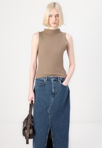 Rjava rebrasta brezrokavnica v kombinaciji z visokim modrim denim krilom z razporkom spredaj. Model drži temno rjavo torbico.
