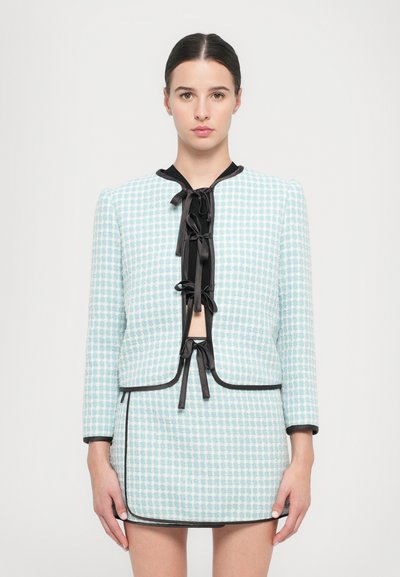 Hellemblau kariertes Jacket mit schwarzem Besatz und Schleifenbindung, kombiniert mit einem passenden Rock. Strukturierter Stoff, taillierte Passform und Dreiviertelärmel.