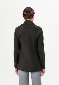 Cardigan in lana verde scuro con colletto a scialle, maniche lunghe e orlo posteriore leggermente allungato. Il tessuto ha una finitura morbida e testurizzata.
