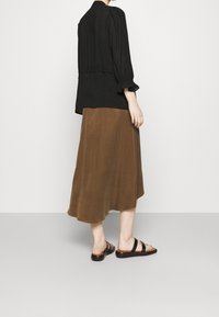 Blouse noire texturée avec des manches bouffantes, associée à une jupe midi marron, complétée par des sandales noires à larges brides, vue de dos.