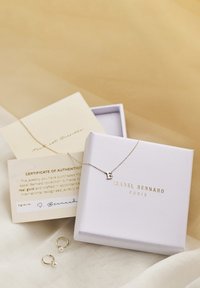 Goldene Halskette mit einem Anhänger in Form des Buchstabens "B" in einer weißen Box, begleitet von einem Echtheitszertifikat und goldenen Ohrringen mit Perlenakzenten.