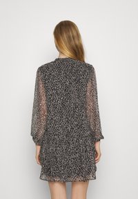 Černé a béžové vzorované šaty s dlouhými, průsvitnými rukávy, nařaseným pasem a volánkovým lemem, vyrobené z lehké, poloprůhledné látky.