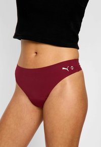 Culotte de bikini bordeaux avec une texture lisse et un design taille basse. Présente un logo blanc et un détail de finition sur un côté.