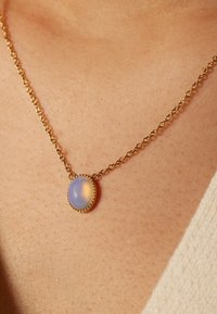 Gouden ketting met een ovaal, lichtblauw stenen hanger. De hanger heeft een parelrand, wat een verfijnd ontwerp creëert.
