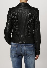 Giubbotto in pelle nera con pannelli testurizzati e borchiati sul retro, vestibilità slim e maniche lunghe, abbinato a jeans in denim blu.