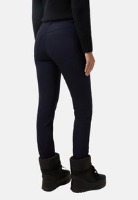 Námořnické modré kalhoty s úzkým střihem, mají zadní kapsy a hladkou texturu, spárované s černými kotníkovými botami s měkkým, izolovaným lemem.