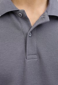 Grå polo t-shirt med et struktureret vaffelmønster, to knapper på kraven og et klassisk kravedesign. Fremstillet af blødt stof.