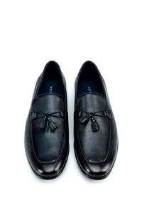 Mocasines de cuero negro con acentos de borlas, que presentan una textura suave y un diseño de punta redonda. Interior forrado en un material oscuro, estilo minimalista.