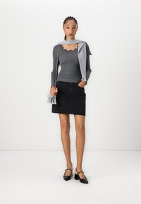 Haut gris à rayures à manches longues avec détail en dentelle, minijupe en denim noire et escarpins noirs avec bride arrière. Écharpe grise drapée sur les épaules.