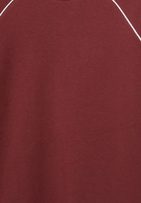 Bordeaux T-shirt gemaakt van zachte katoen, met een ronde halslijn en contrasterende witte piping langs de schouders. Gladde textuur.