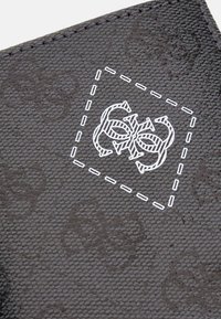 Portafoglio nero in tessuto con una spessa outline bianca cucita in evidenza e un logo decorativo al centro. Materiale resistente con un motivo dettagliato.