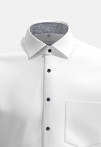 Camicia bianca con colletto strutturato, fodera interna a motivo floreale blu e quattro bottoni scuri. Presenta una tasca sul petto.