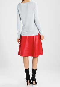 Suéter texturizado azul claro, falda de cuero roja con diseño acampanado y botines negros hasta el tobillo. El suéter tiene un escote redondo y mangas largas.