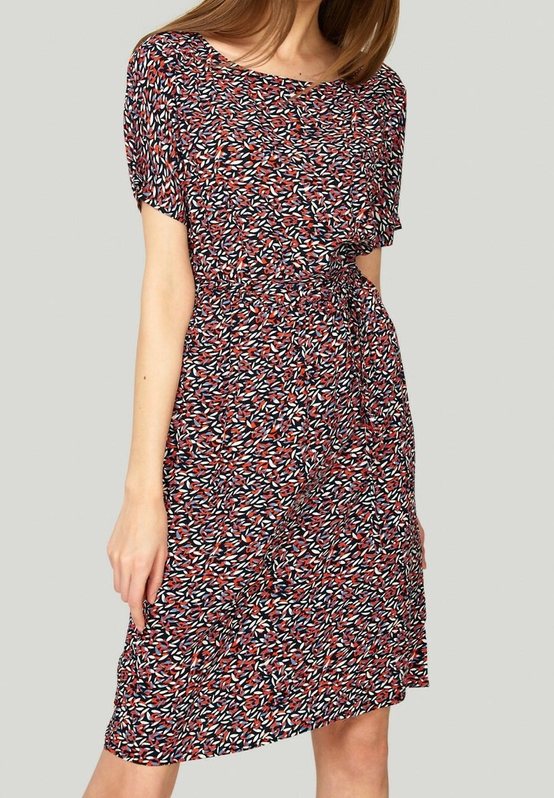 Kukkakuvioinen mekko, jossa on lyhyet hihat ja punaisia, valkoisia ja sinisiä värejä. Vyötäröllä solmittava yksityiskohta, polvipituinen, kevyt kangas, rento istuvuus.