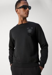 Sudadera negra de manga larga y cuello redondo, con un gráfico de Mickey Mouse a cuadros en el pecho y una textura de tela suave.