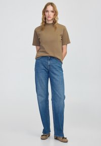 Bruine kortek mouwen shirt en lichtblauwe rechte jeans. Het shirt heeft een ronde hals, terwijl de jeans traditionele zakken en naden hebben.