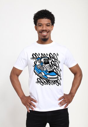 Smilende mand med krøllet hår iført en hvid t-shirt med en blå og sort sneaker-grafik med graffiti-stil baggrund.
