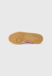 Adidas tenisica s potplatom, koji ima teksturirani dizajn od gume u boji smole s kružnim uzorkom i utisnutim logom. Dominantne boje: bež s ružičastim naglascima.