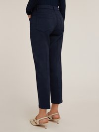 Mörkblå byxor med skräddarsydd passform, med två bakfickor och uppvikta benen, i kombination med ljusa klackskor.