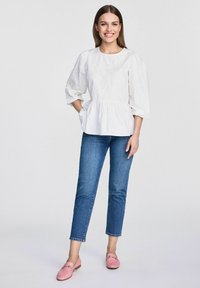 Biała bluzka peplum z krótkimi bufkami, zestawiona z niebieskimi dżinsami i różowymi loafersami z dekoracyjnym akcentem.