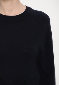 Dunkelblauer Pullover aus weichem Strickstoff, mit rundem Ausschnitt und gerippten Bündchen, in leicht lockerer Passform und minimalistischem Design.