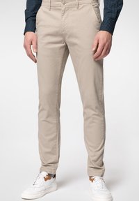 Beiga bomullschinos med slim fit, med sidofickor, en bakficka och bärs med vita sneakers och en mönstrad skjorta.