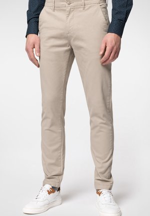 Cino in cotone beige con una vestibilità slim, dotato di tasche laterali, una tasca posteriore singola e indossati con sneakers bianche e una camicia a fantasia.