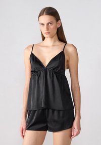 Fekete selyem camisole top vékony pántokkal, mély V-nyakkivágással, ráncolt derékkal és laza fazonnal. Összepárosítva az ugyanolyan fekete selyem sorttal.