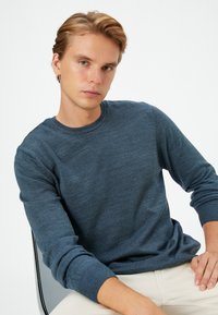 Blauer Strickpullover mit Rundhalsausschnitt und langen Ärmeln, ausgestattet mit gerippten Bündchen und Saum, auf einem neutralen Hintergrund präsentiert.