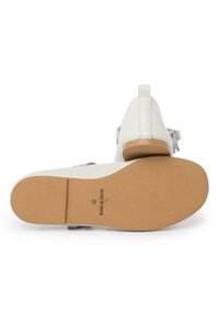 Scarpa bianca in pelle con tacco basso, suola in gomma e una cintura decorativa. L'interno è dotato di una morbida fodera e dettagli di cucitura sottili.