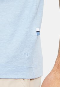 Camicia azzurro chiaro a maniche corte realizzata in tessuto morbido, con una finitura texturizzata e un piccolo etichetta con strisce blu e bianche sul lato.