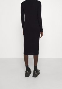 Vestito a maglia nera a coste con lunghezza midi e maniche lunghe, caratterizzato da una sottile fessura all'orlo. Abbinato a sneakers nere e calze.