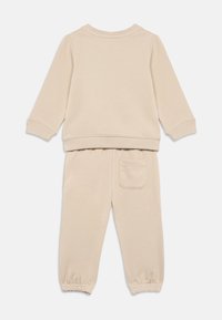 Set di felpa a maniche lunghe e pantaloni beige con polsini a coste, caviglie elastiche e una sola tasca sul retro dei pantaloni.