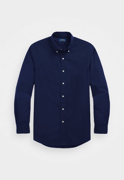 Mörkblå knapp-up skjorta i bomull. Har en klassisk krage, långa ärmar och vita knappar framtill och vid ärmsluten.