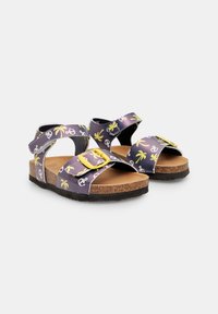 Lillasest sandaalid kollase kinnitusega, mille rihmadel on palmipuude ja ankrute muster. Kork jalatsi sisemus ja must tekstureeritud kummitald.