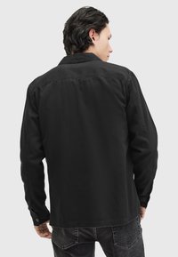Schwarze Jeanshemd mit Kragen und Knopfausschnitten, im lässigen Schnitt und mit sichtbaren Nähten auf der Rückseite.