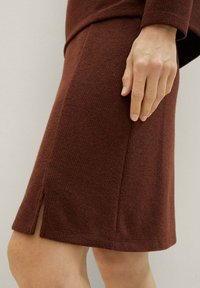 Pletená hnědá sukně s texturovanou tkaninou, bočním rozparkem pro pohodlný pohyb a těsným pasem.