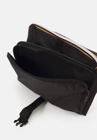 Schwarze Stofftasche mit einem Reißverschluss, ausgestattet mit einer Innentasche und einem farbigen Akzent entlang des Reißverschlusses. Texturiertes Material und langlebiges Design.