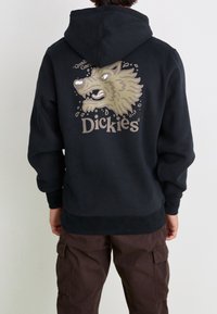 Sweat à capuche noir arborant un graphisme de loup aux couleurs beige et blanc. La marque "Dickies" est affichée en blanc en dessous.
