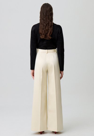 Pantalons larges crème avec une texture lisse, taille haute et passants de ceinture, associés à un haut noir ajusté à manches longues.