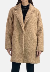 Beżowy, teksturowany płaszcz z imitacji futra z wyciętym kołnierzem, zapięciem na jeden guzik i dwoma bocznymi kieszeniami. Luźny fason z długimi rękawami.