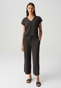 Ensemble noir texturé en deux pièces, composé d'un haut à col en V avec manches courtes et d'un pantalon à cordon de serrage à coupe décontractée. Porté avec des sandales noires.