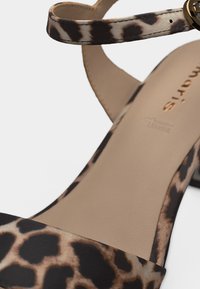 Sandale pour femme avec des brides imprimé léopard, une semelle intérieure beige rembourrée et une petite boucle dorée sur la bride de cheville.