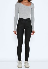 Grå långärmad tröja med vid halsringning, kombinerad med högmidjade svarta skinny jeans. Vita sneakers med beige detaljer fulländar outfiten.