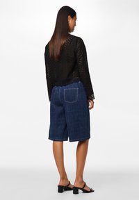 Top a maglia nera traforata con maniche lunghe, abbinato a pantaloni corti in denim blu fino al ginocchio con tasche posteriori e una vestibilità dritta.