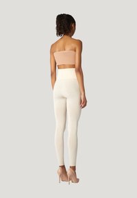 Top strapless beige e leggings a vita alta crema, realizzati in tessuto elasticizzato morbido. La modella indossa tacchi alti di colore chiaro.