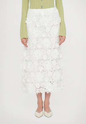 Witte kant midi rok met bloemen uitsnijdingen en gedetailleerde versieringen, gecombineerd met een groene ribbed blouse met lange mouwen en crèmekleurige spitse flats.